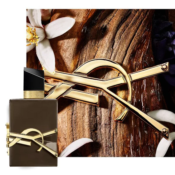 Libre Santal Couture glazed brown bottle on sandalwood bark with golden Cassandre and white flowers.