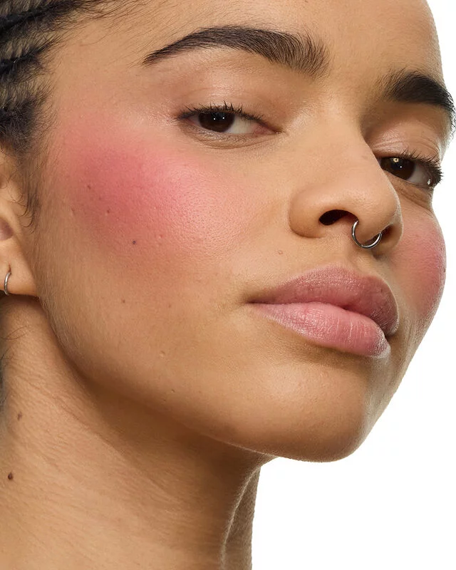Close-up of a model holding the YSL Make Me Blush Lifted Glow Cream Blush in shade #54 Berry Bang, showcasing a radiant, lifted glow on her cheekbones.