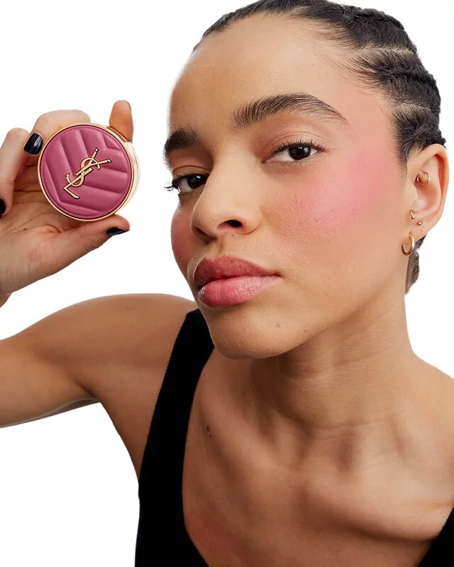 Close-up of a model holding the YSL Make Me Blush Lifted Glow Cream Blush in shade #54 Berry Bang, showcasing a radiant, lifted glow on her cheekbones.