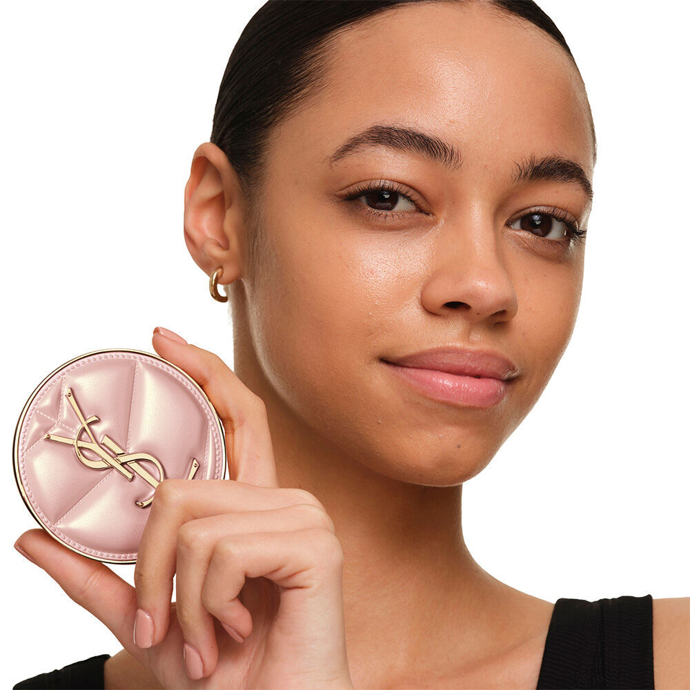 Model with a smooth, radiant complexion holding the pink YSL SKIN AFFAIR CUSHION FOUNDATION to showcase a naturally glowing, flawless skin finish.