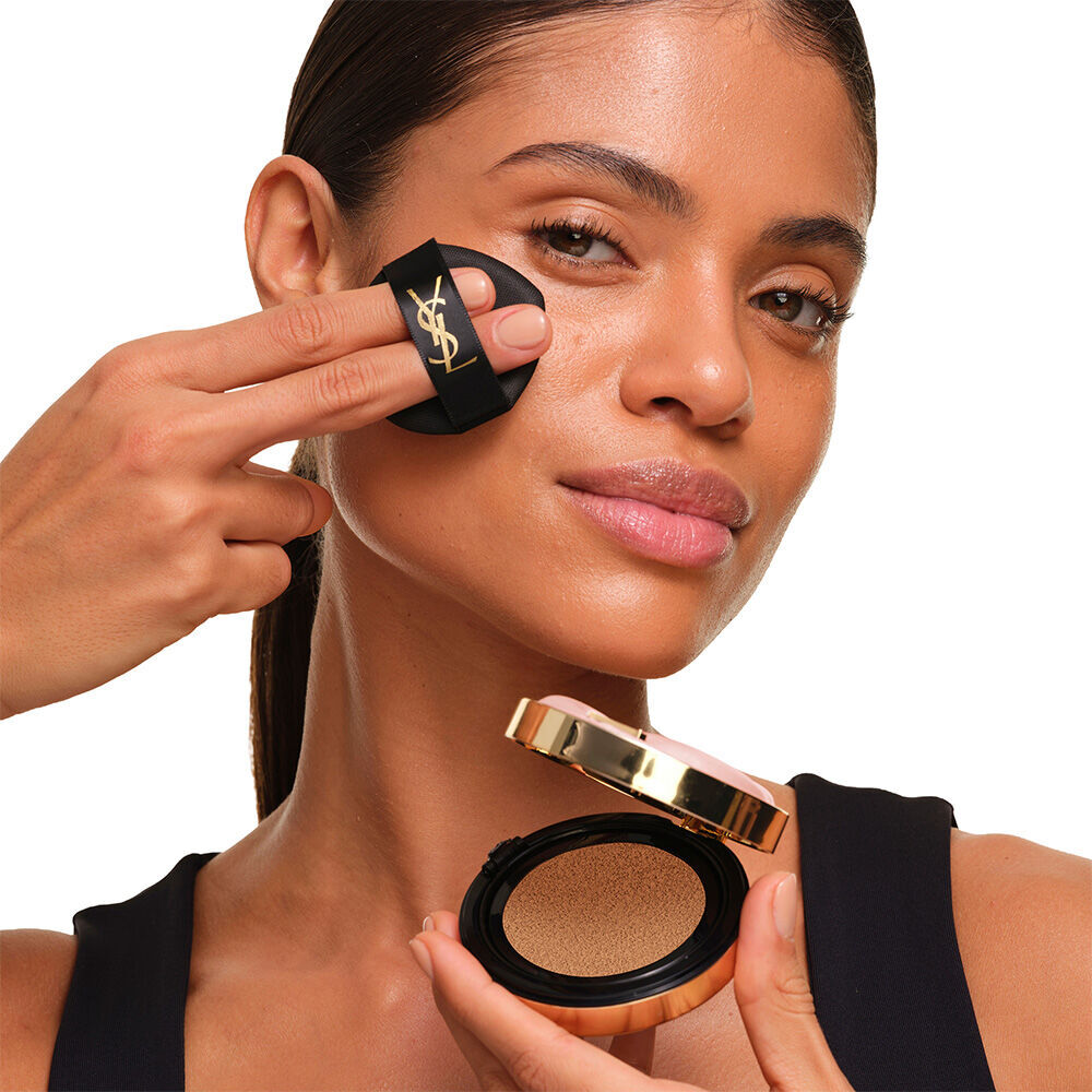 Model with a smooth, radiant complexion holding the pink YSL SKIN AFFAIR CUSHION FOUNDATION to showcase a naturally glowing, flawless skin finish.