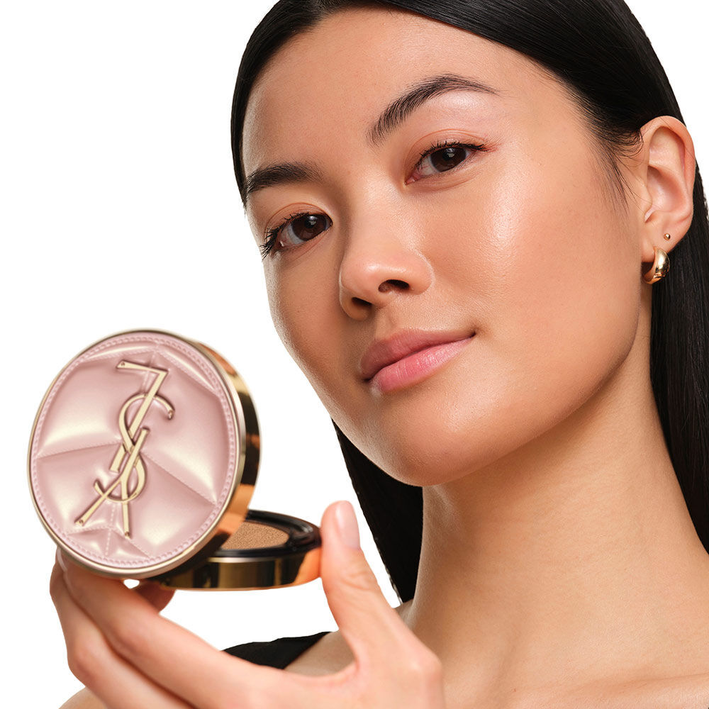 Model with a smooth, radiant complexion holding the pink YSL SKIN AFFAIR CUSHION FOUNDATION to showcase a naturally glowing, flawless skin finish.