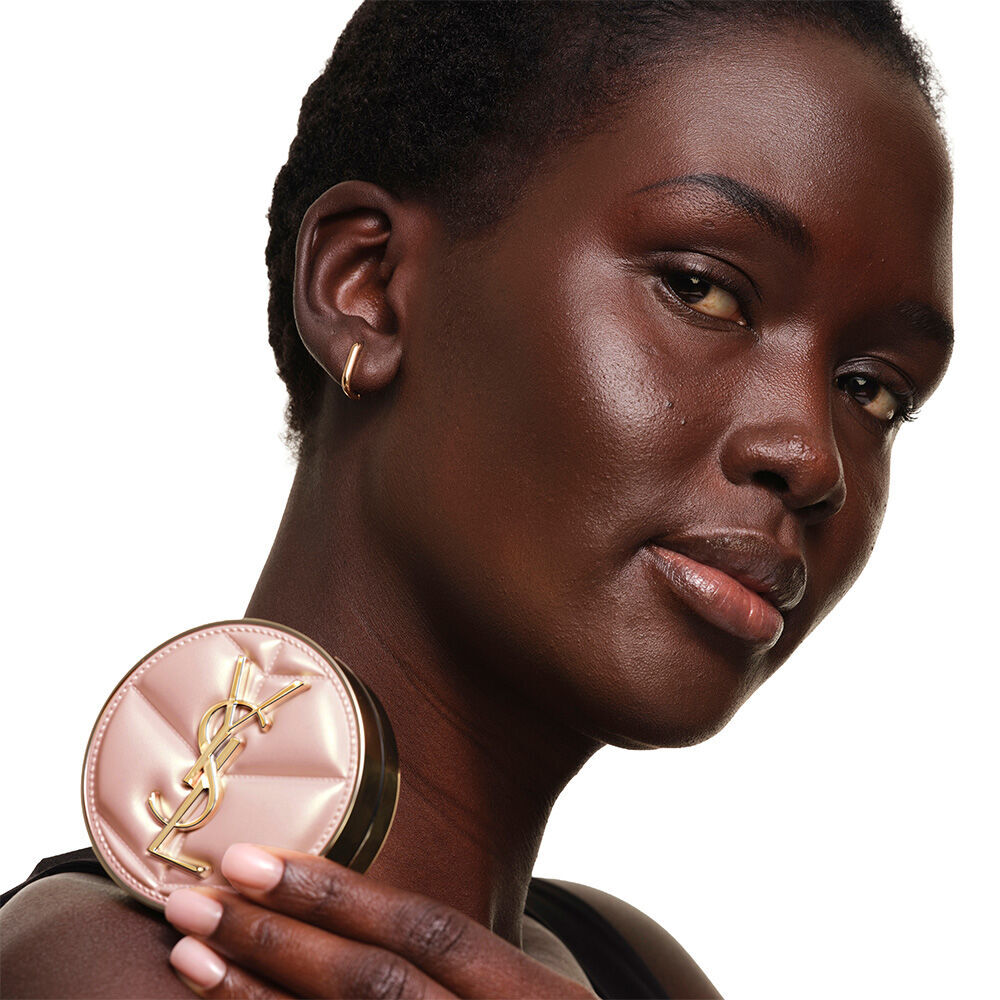 Model with a smooth, radiant complexion holding the pink YSL SKIN AFFAIR CUSHION FOUNDATION to showcase a naturally glowing, flawless skin finish.