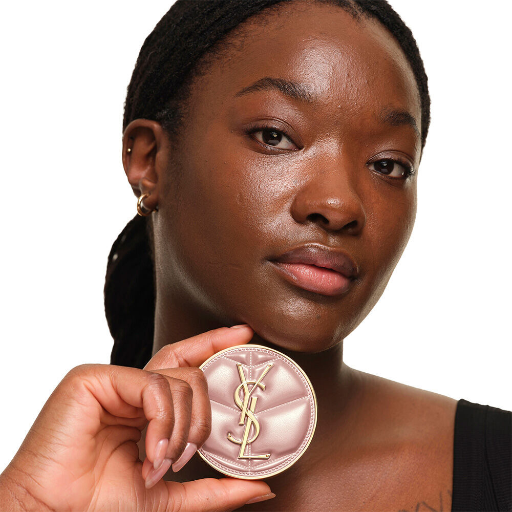 Model with a smooth, radiant complexion holding the pink YSL SKIN AFFAIR CUSHION FOUNDATION to showcase a naturally glowing, flawless skin finish.
