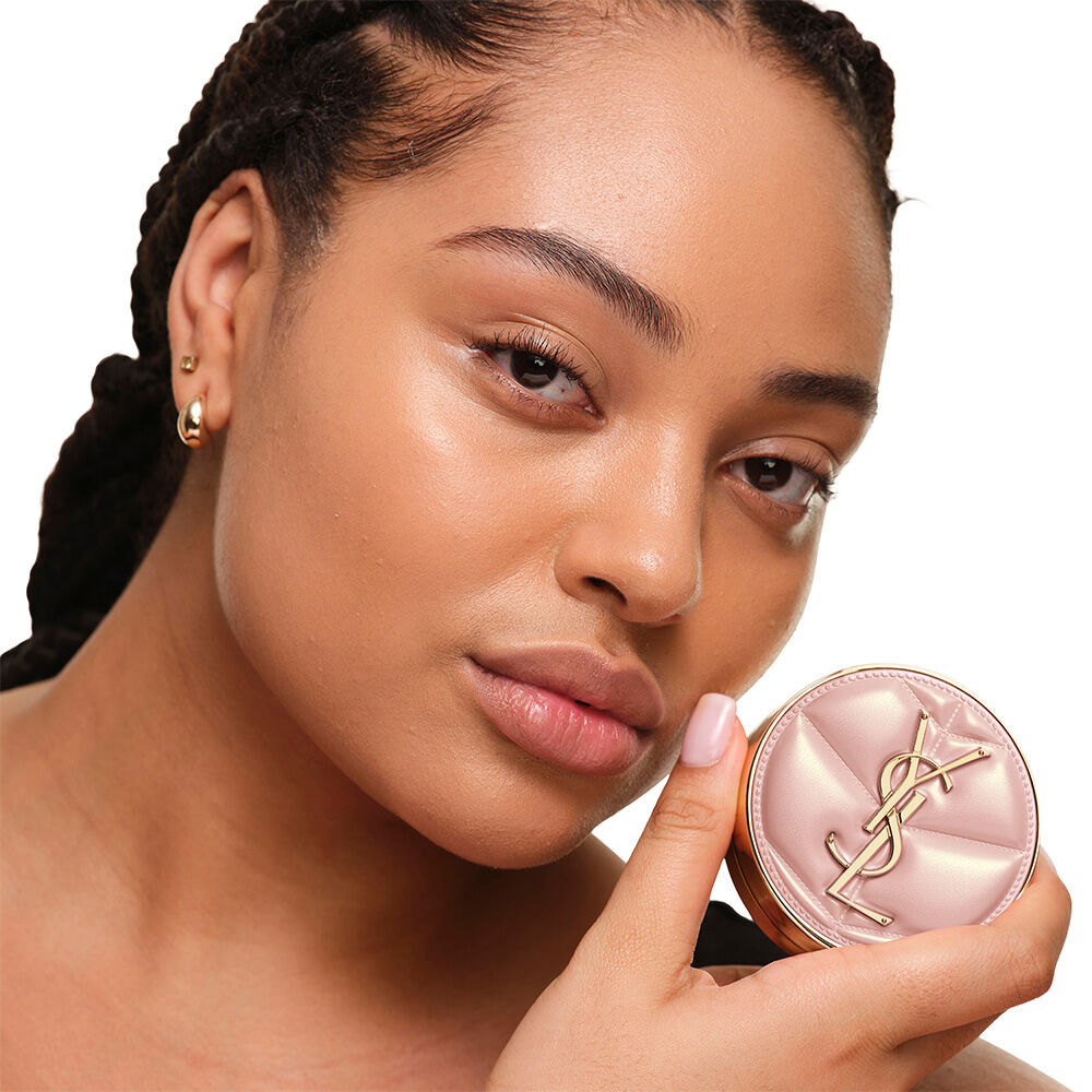 Model with a smooth, radiant complexion holding the pink YSL SKIN AFFAIR CUSHION FOUNDATION to showcase a naturally glowing, flawless skin finish.