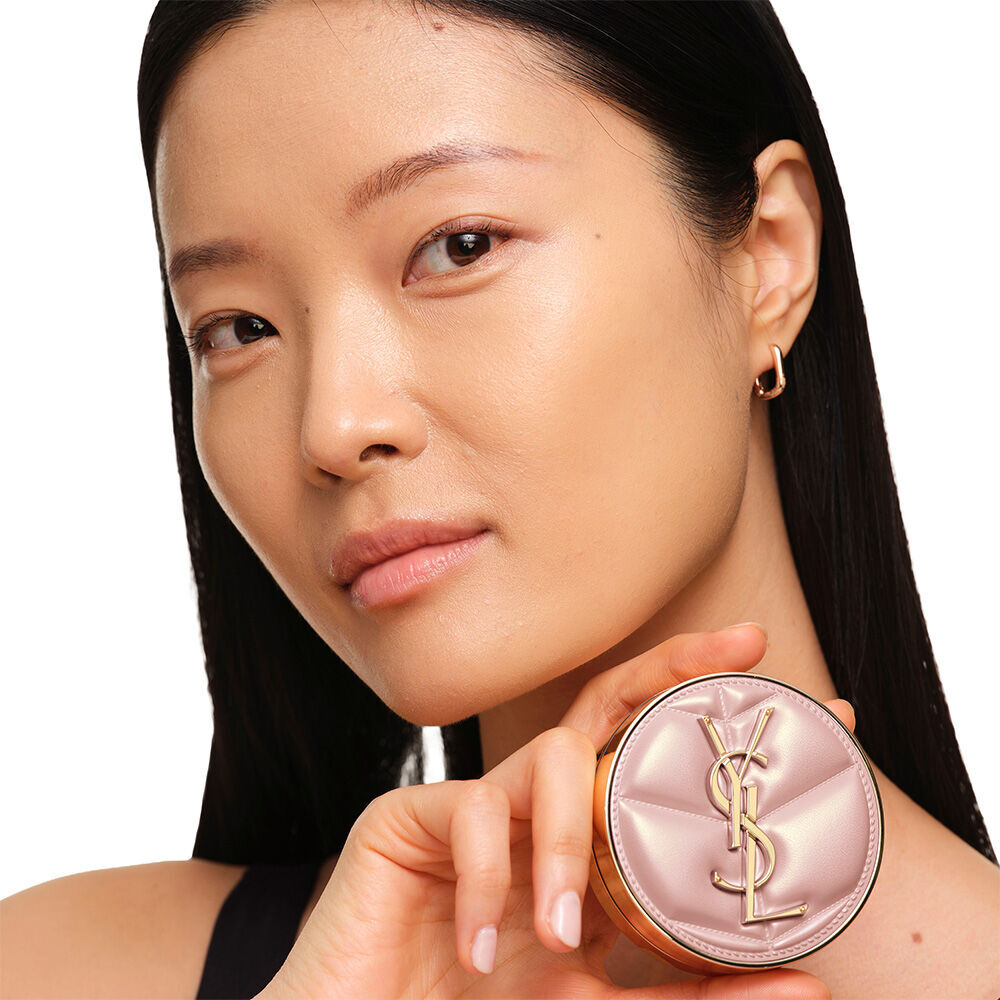 Model with a smooth, radiant complexion holding the pink YSL SKIN AFFAIR CUSHION FOUNDATION to showcase a naturally glowing, flawless skin finish.