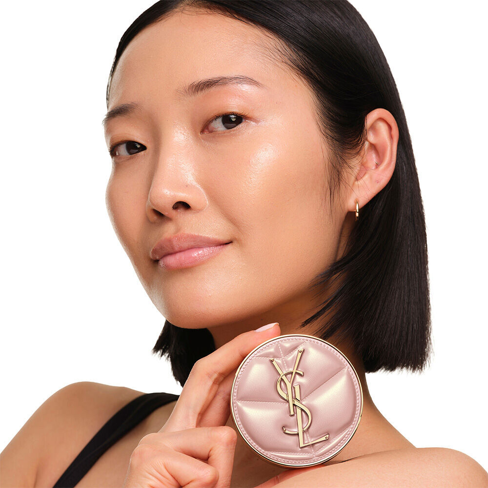 Model with a smooth, radiant complexion holding the pink YSL SKIN AFFAIR CUSHION FOUNDATION to showcase a naturally glowing, flawless skin finish.