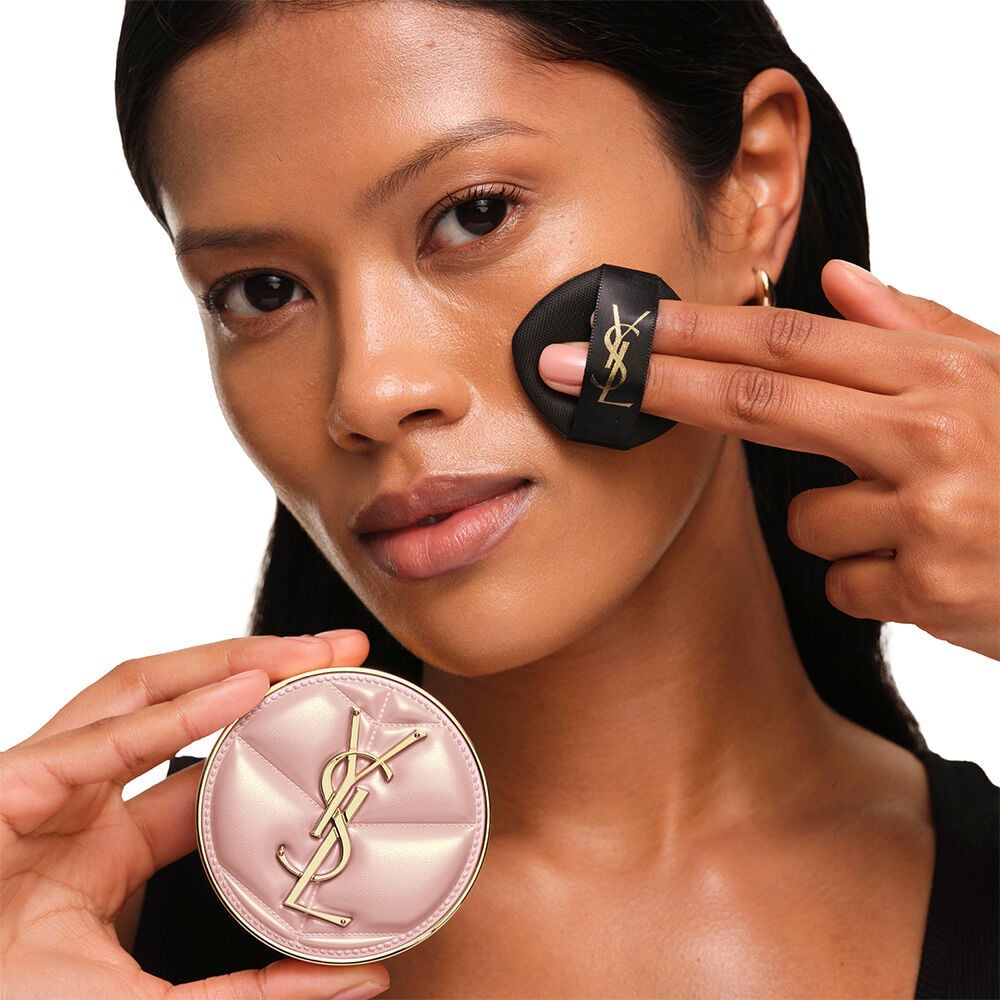 Model with a smooth, radiant complexion holding the pink YSL SKIN AFFAIR CUSHION FOUNDATION to showcase a naturally glowing, flawless skin finish.