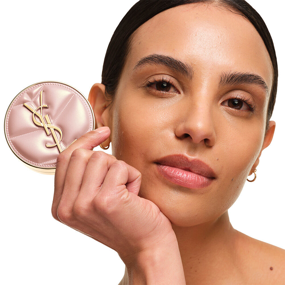 Model with a smooth, radiant complexion holding the pink YSL SKIN AFFAIR CUSHION FOUNDATION to showcase a naturally glowing, flawless skin finish.