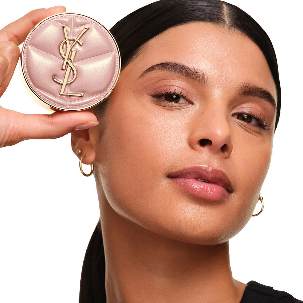 Model with a smooth, radiant complexion holding the pink YSL SKIN AFFAIR CUSHION FOUNDATION to showcase a naturally glowing, flawless skin finish.