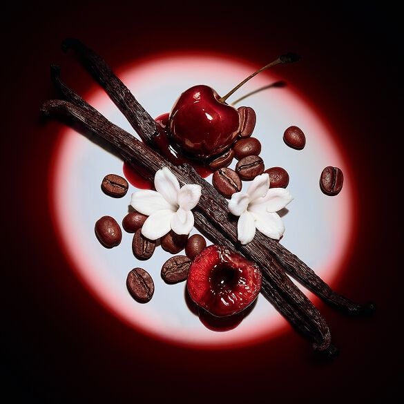 Close-up of juicy red cherries, jasmine flowers, vanilla pods, and coffee beans highlighted by a dramatic spotlight for Black Opium Eau de Parfum Over Red.
