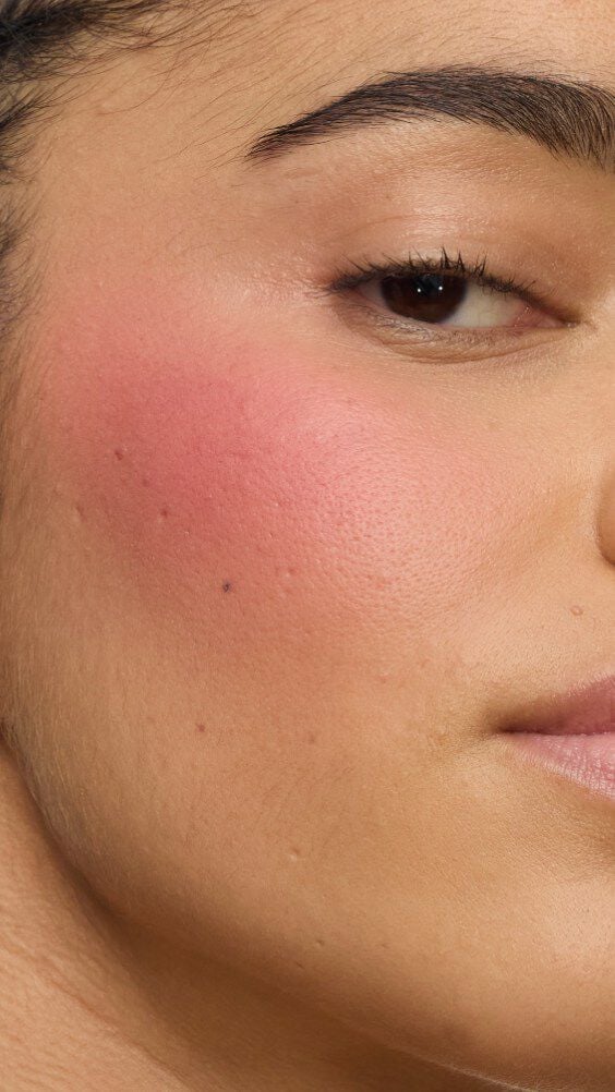 Close-up of a model's cheek wearing the Make Me Blush routine: Powder #54 Berry Bang layered with Cream #44 Nude Lavallière for a vibrant, custom pink statement.