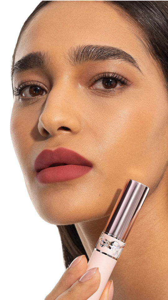 Le mannequin Merna portant le YSL LOVENUDE Lip Blusher en teinte 4, tenant le produit près de ses lèvres nude rosées.