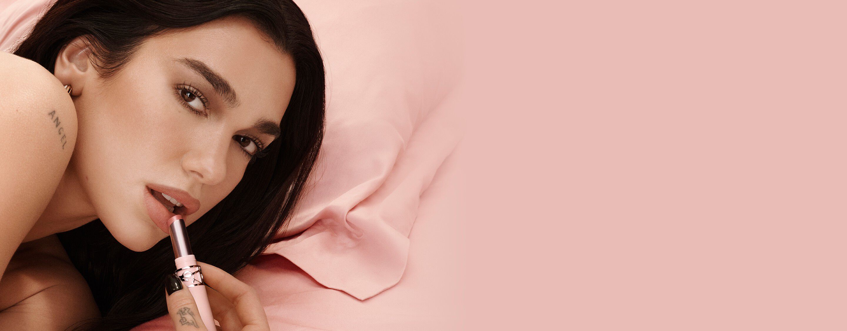 Dua Lipa, ambassadrice YSL Beauty, appliquant le YSL LOVENUDE Lip Blusher en teinte 44, sur un fond rose tendre.