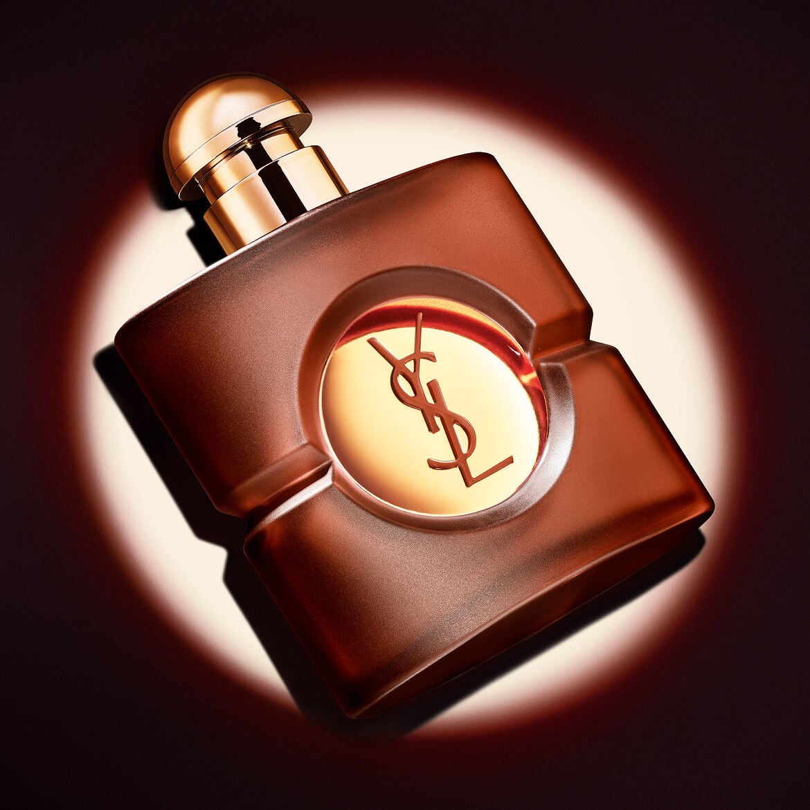 Flacon carré de parfum OPIUM d&rsquo;YSL en verre dépoli brun avec son bouchon doré, présenté en diagonale sous un faisceau lumineux circulaire net.