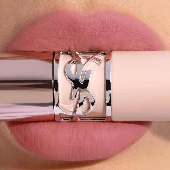 Gros plan sur des lèvres portant le YSL LOVENUDE LIP BLUSHER en teinte 44, avec un tube de rouge à lèvres YSL rose pâle et une bague Cassandre argentée.
