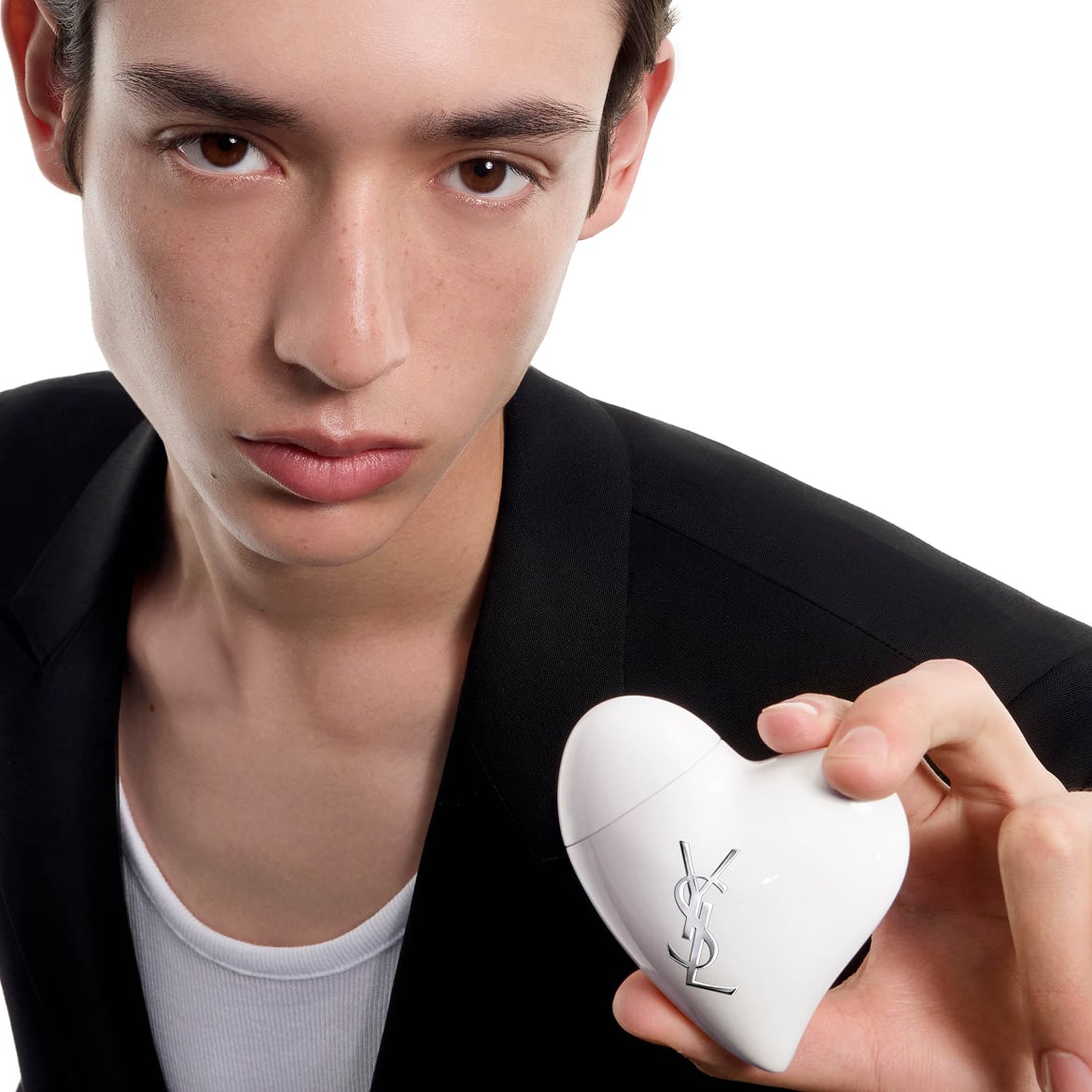 Gros plan d'un homme en blazer noir tenant le produit CARE CRUSH blanc en forme de cœur. Fond blanc.