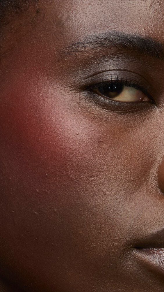 Close-up of a model's cheek wearing the Make Me Blush routine: Powder #15 Chili Crush layered with Cream #65 Strawberry Seduction for a bold, post-workout glow.