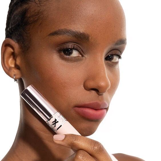 Le mannequin Zahara portant le YSL LOVENUDE Lip Blusher en teinte 7, tenant le produit près de ses lèvres nude rosées.