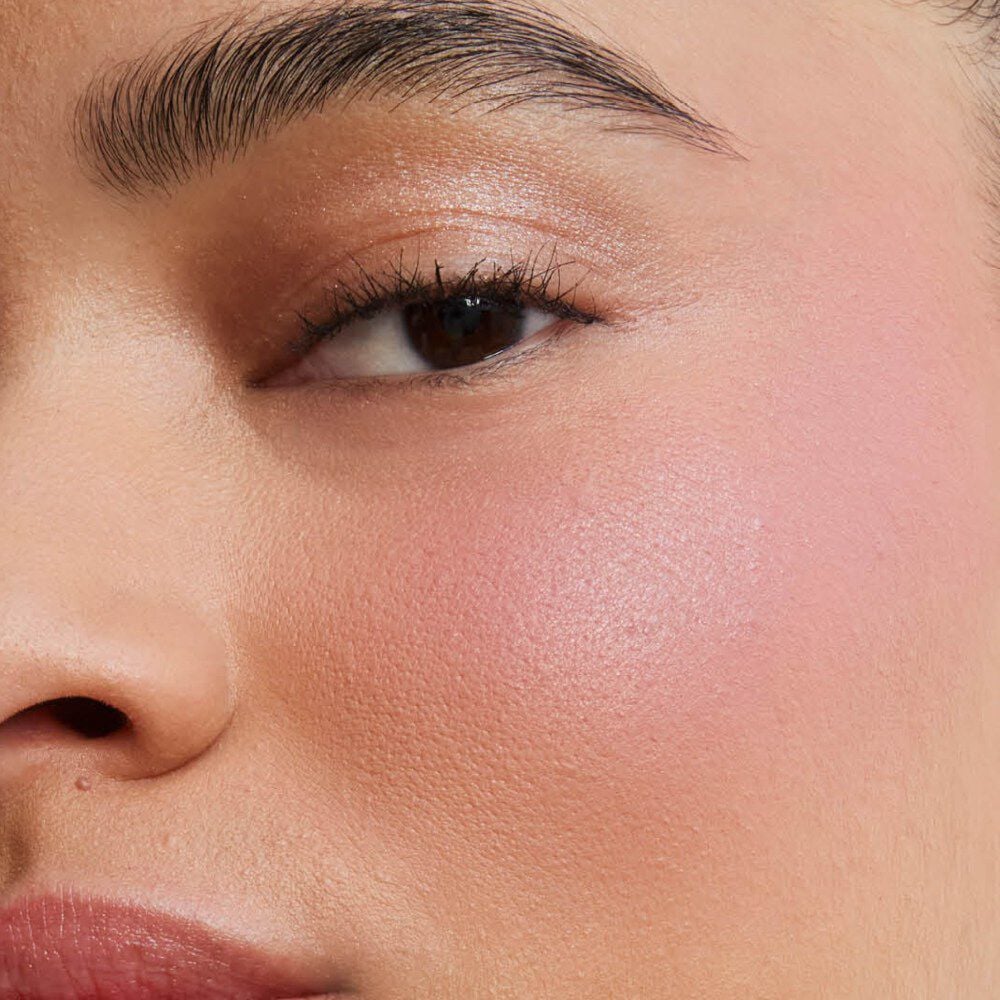 Close-up of a model's cheek showcasing the soft-focus, airbrushed matte finish of Make Me Blush Powder in shade #44 for a buildable, blurred color flush.